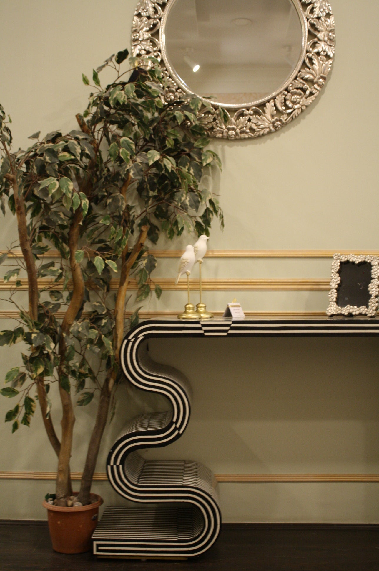 Monochrome twist black and white striped table with unique curved design beside potted plant and decorative mirror